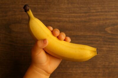A person's hand with a slight yellow or orange tint, holding a banana.